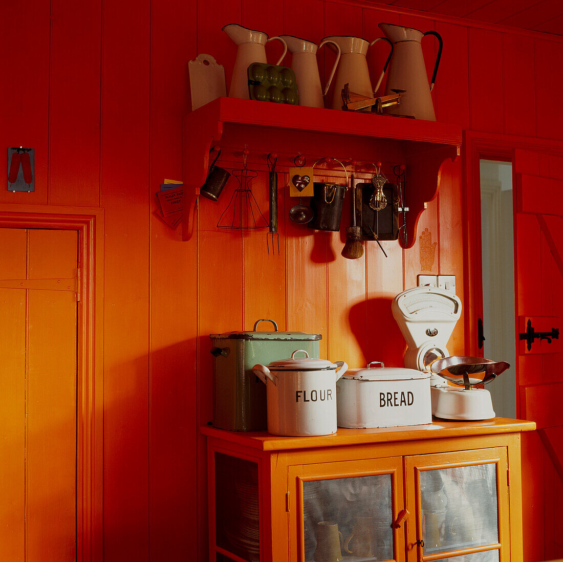 Ecke einer in leuchtendem Orange gestrichenen Landhausküche mit Vintage-Schränken und -Geschirr
