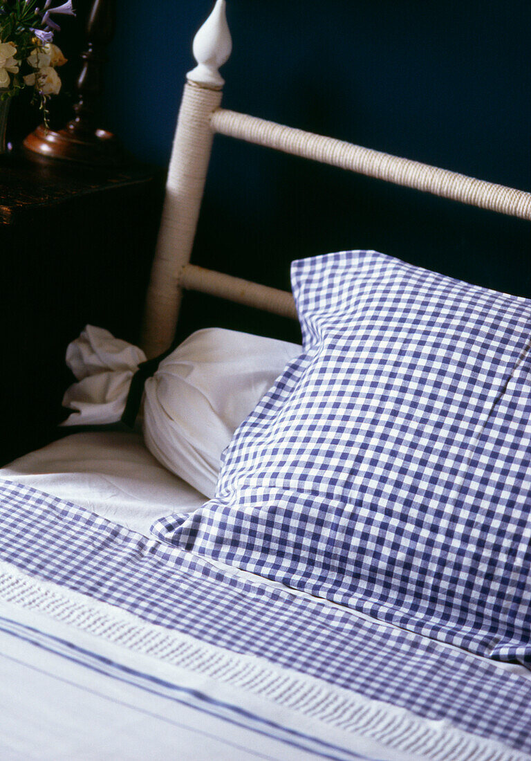 Detail of blue and white gingham bed linen and bolster pillow on a bed