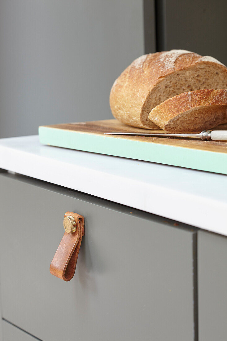 Aufgeschnittenes Brot auf Brett mit Messer und Lederbeschlag auf Küchenschublade London UK