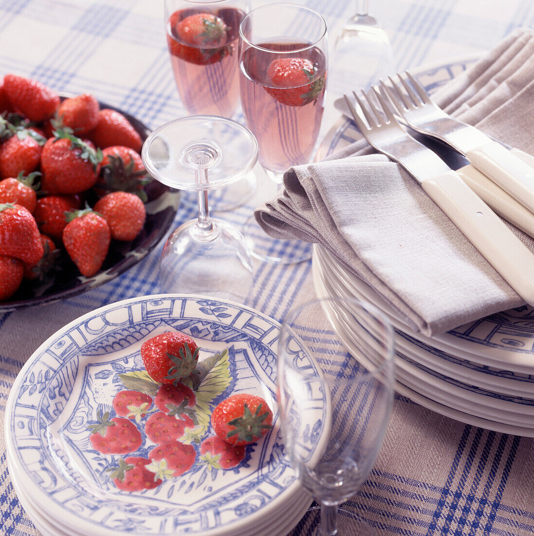 Table top with blue and white crockery and table linen with glasses and strawberries