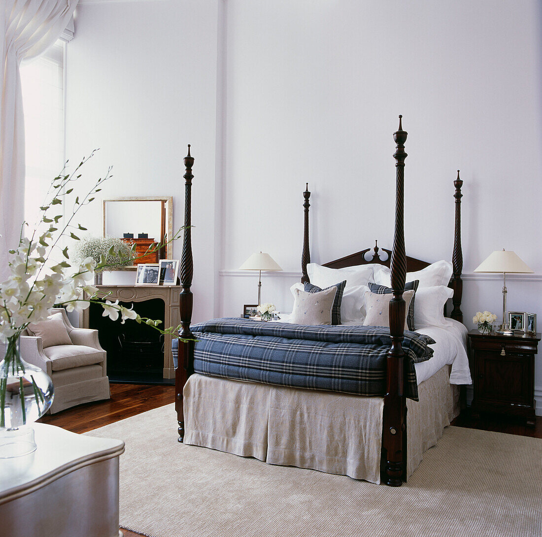 Himmelbett mit Bettwäsche in einem großen weißen Schlafzimmer mit frischen Blumen