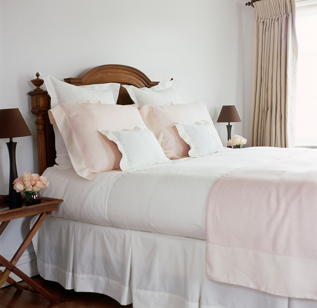 Nahaufnahme eines Vintage-Holzbettes mit rosa und weißer feiner Bettwäsche