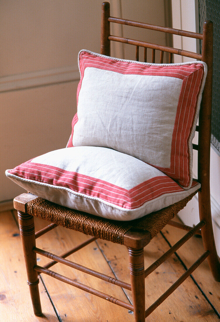 Single antique dining chair with red and cream linen cushions on waxed floorboards