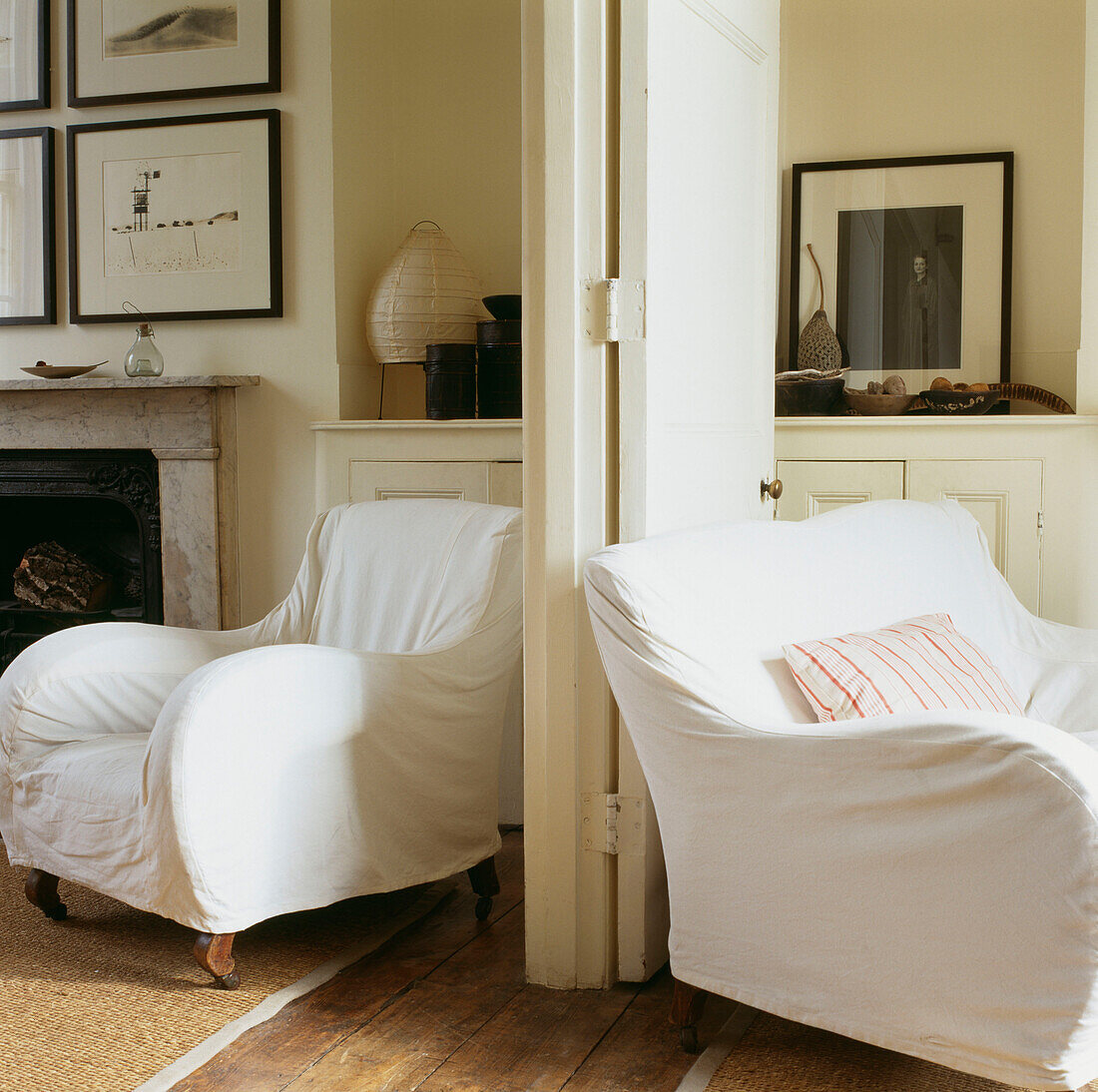 Sessel mit losen Bezügen aus weißem Kattun auf beiden Seiten der Wohnungstür im Wohnzimmer