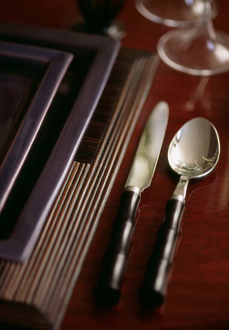 Besteck mit Bambusgriff und schwarzer, quadratischer Teller auf Bambusmatte auf Esstisch (Detailaufnahme)