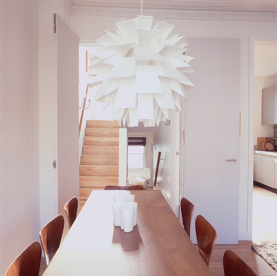 Modernes, offenes Esszimmer mit großer weißer Deckenleuchte über langem Esstisch mit Stühlen aus Sperrholz
