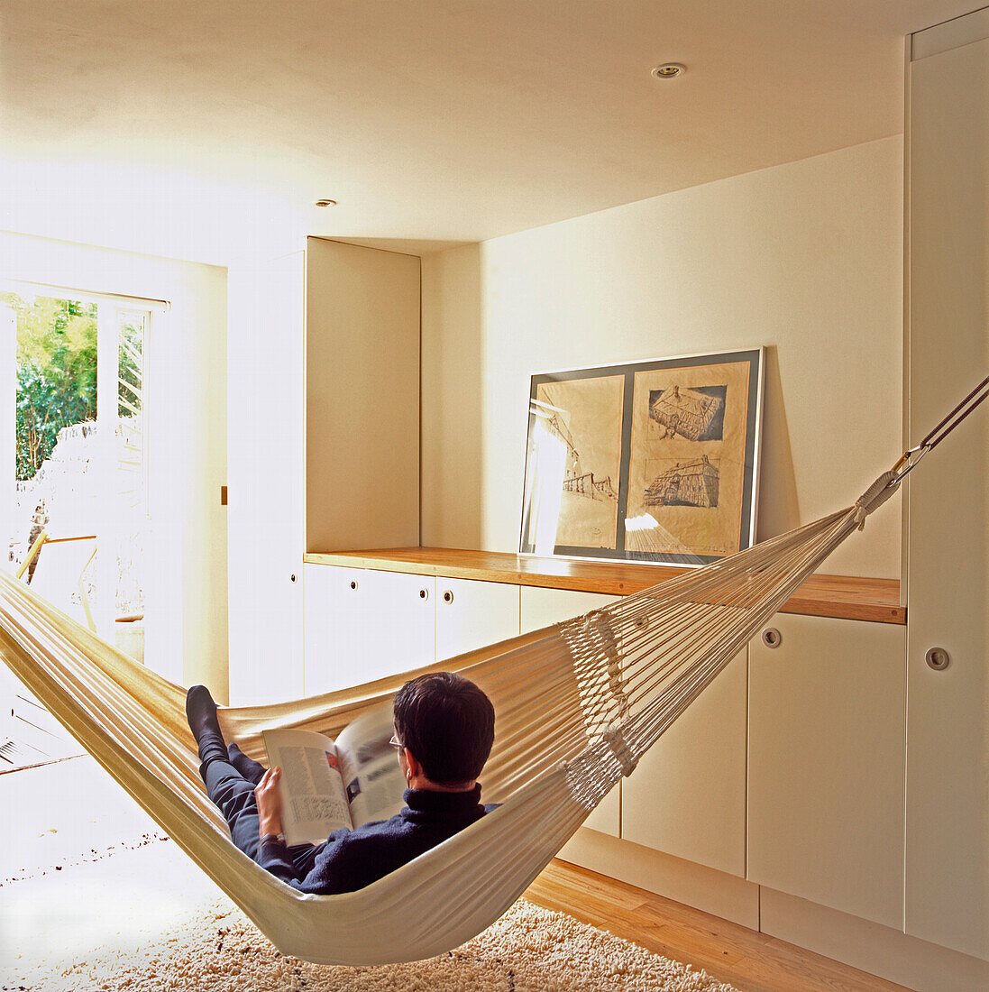 Man reading in white cotton hammock in lobby area with storage cupboards