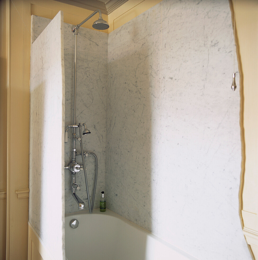 Nahaufnahme der Duschwand aus Carrara-Marmor über der Badewanne im cremefarbenen Badezimmer
