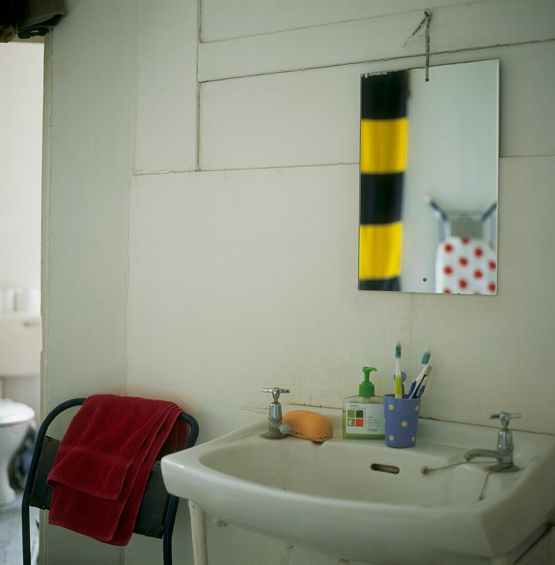 Tableaux in weißem Badezimmer mit Metallstapelstuhl und Spiegelreflexionen über dem Waschbecken