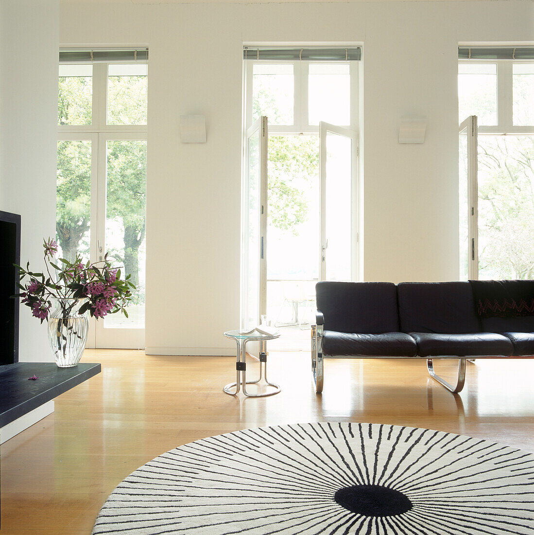 Geräumiges Wohnzimmer mit einem schwarz-weißen, kreisförmigen Sunburst-Teppich und schwarzen Ledermöbeln aus den 60er Jahren