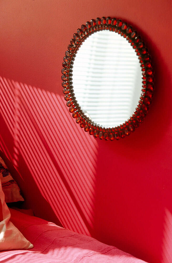 Runder Spiegel mit rotem Zierrahmen auf magentafarbenen Wänden in einem Jugendzimmer