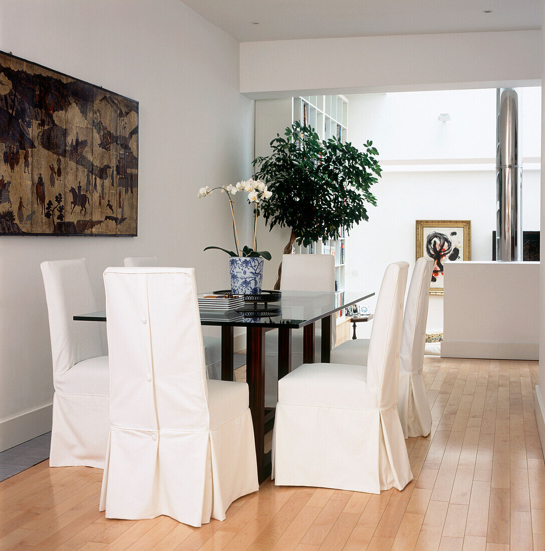 Modernes weißes offenes Esszimmer mit Holzfußboden, Glastisch und losen Bezügen für die Esszimmerstühle