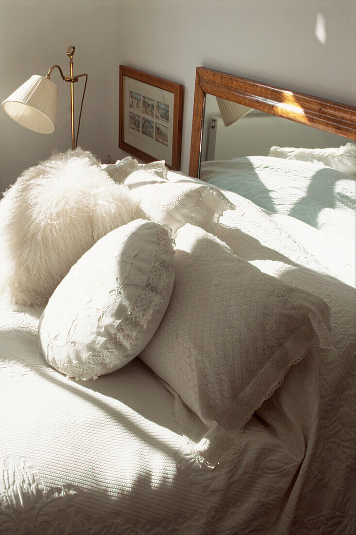 White bed linen and cushions on a single bed with a mirror headboard