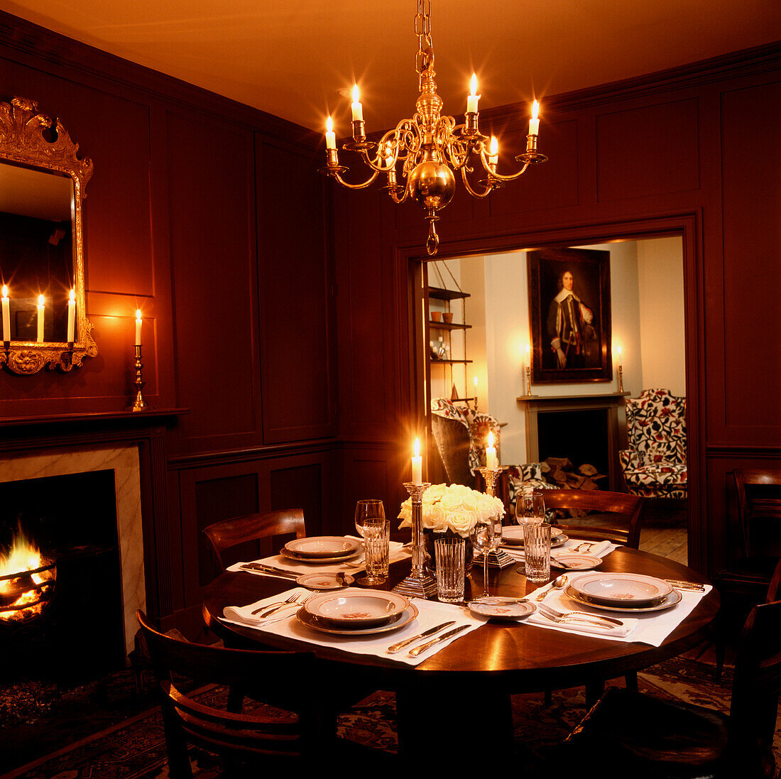 Candlelit dinner set in reddish brown wood panelled dining room with views of the wing armchairs in sitting room