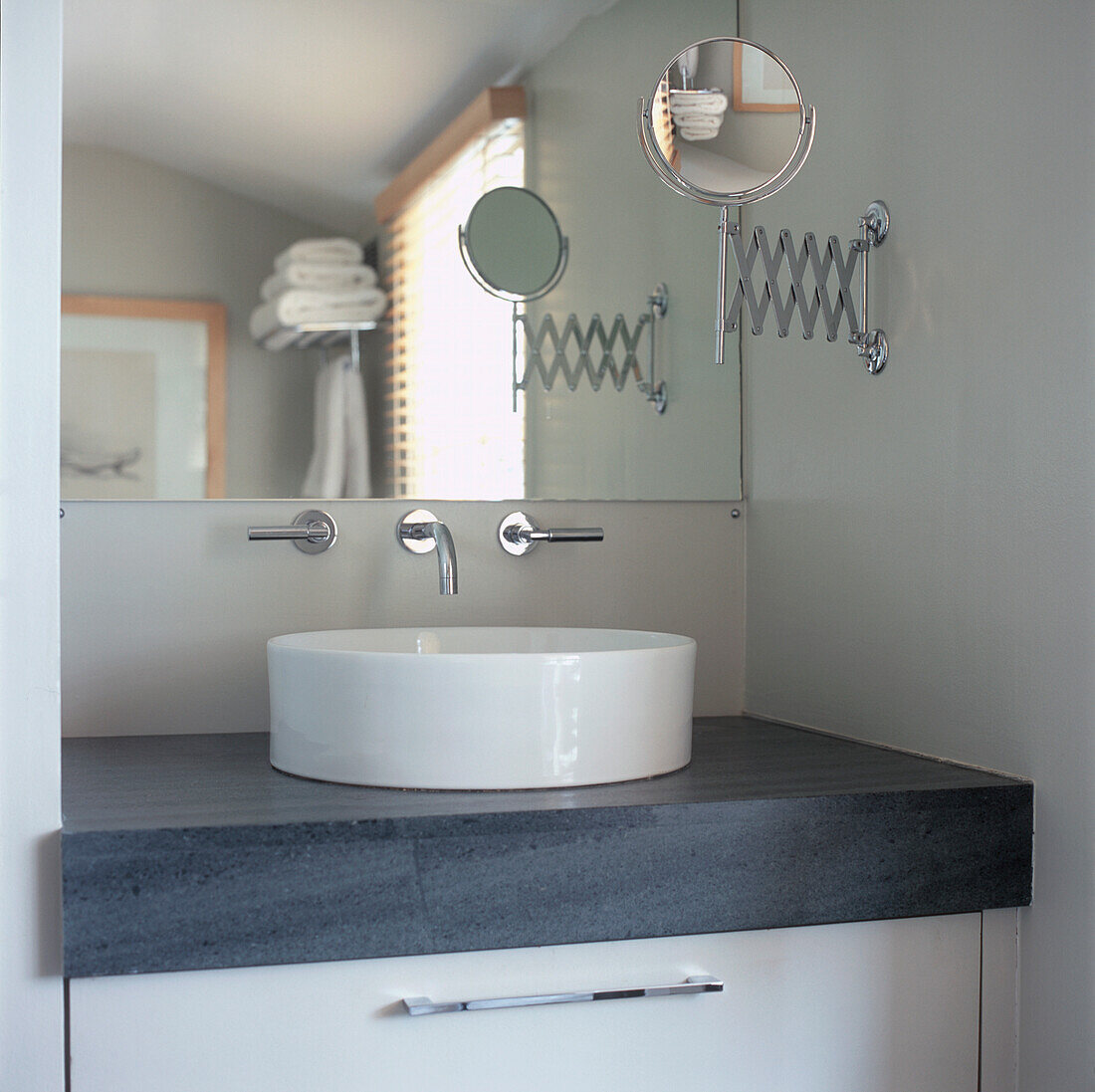 Nahaufnahme eines weißen Keramikwaschbeckens auf grauem Marmor mit großem Spiegel in einem modernen Badezimmer