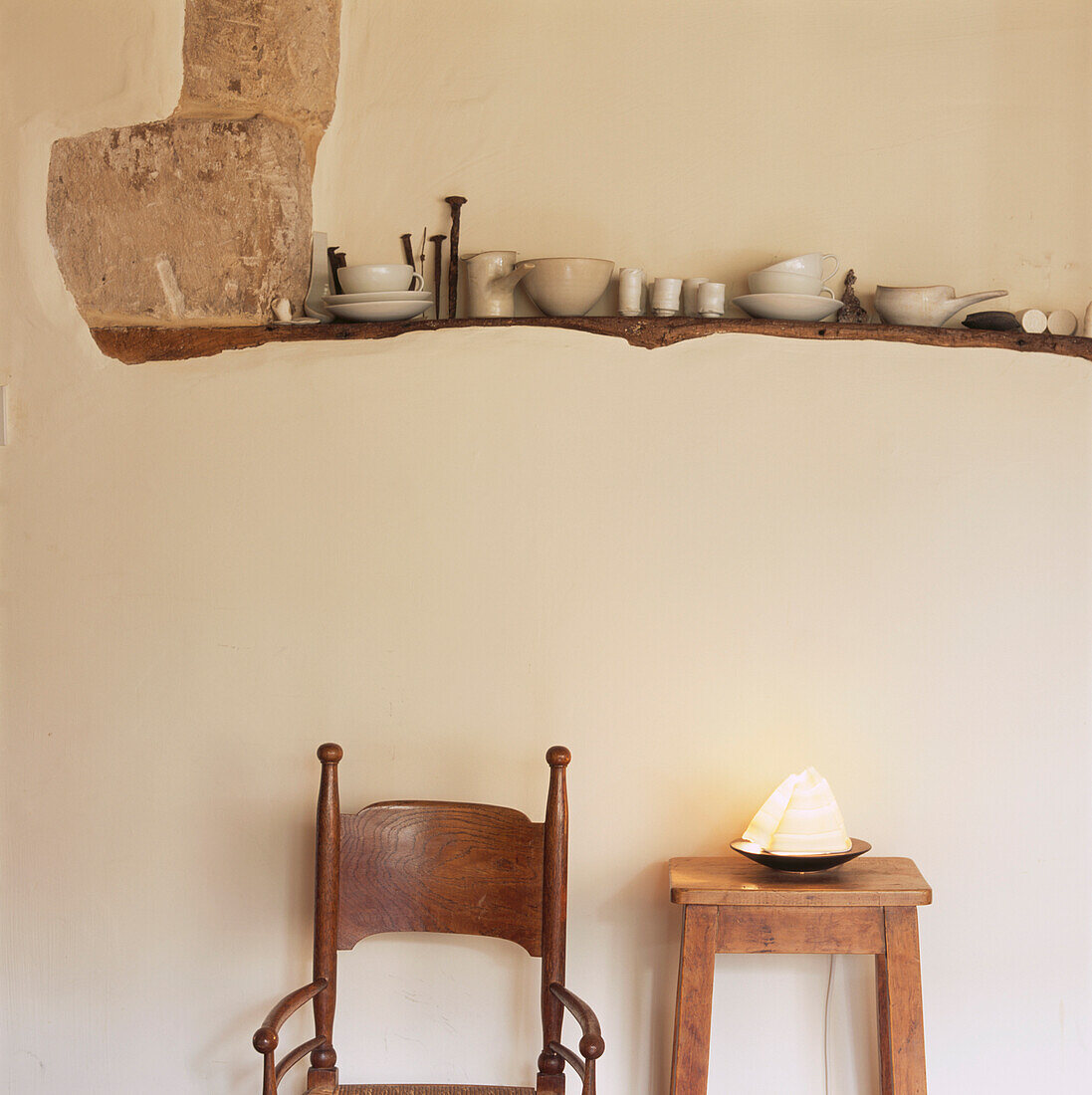 Glasierte Keramik auf einem Holzbalken in einer verputzten Wand über einem Holzsessel und einem Hocker