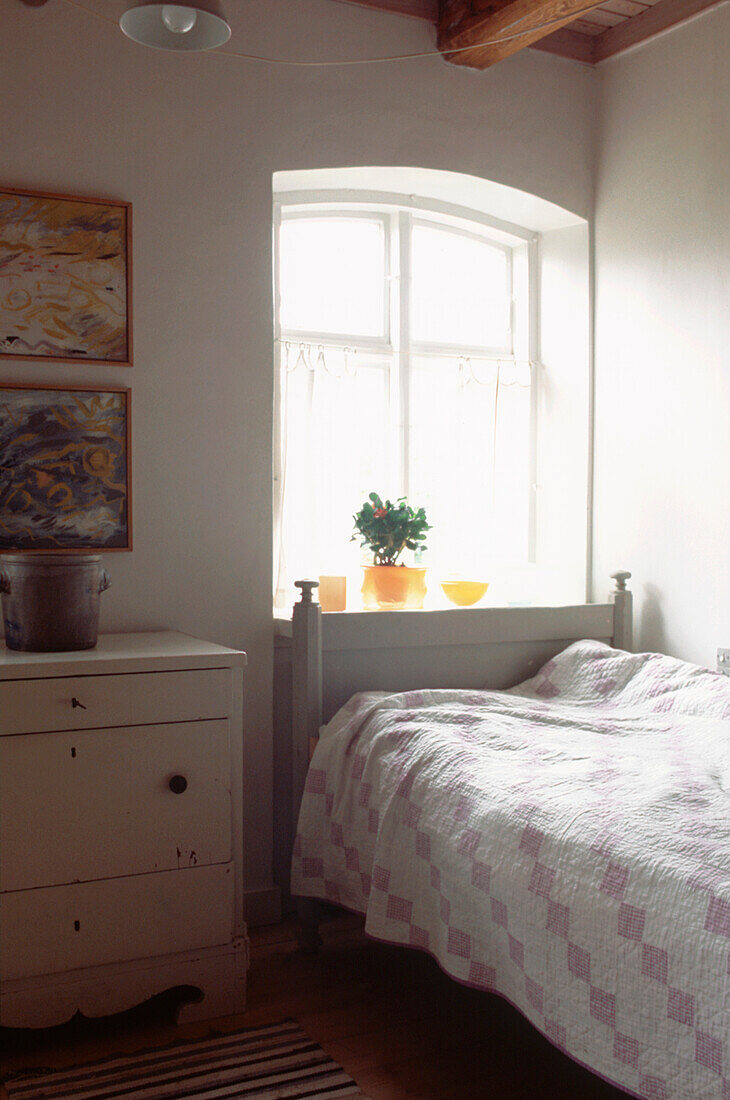 Small white modern country style single bedroom with bed chest of draws and arched window