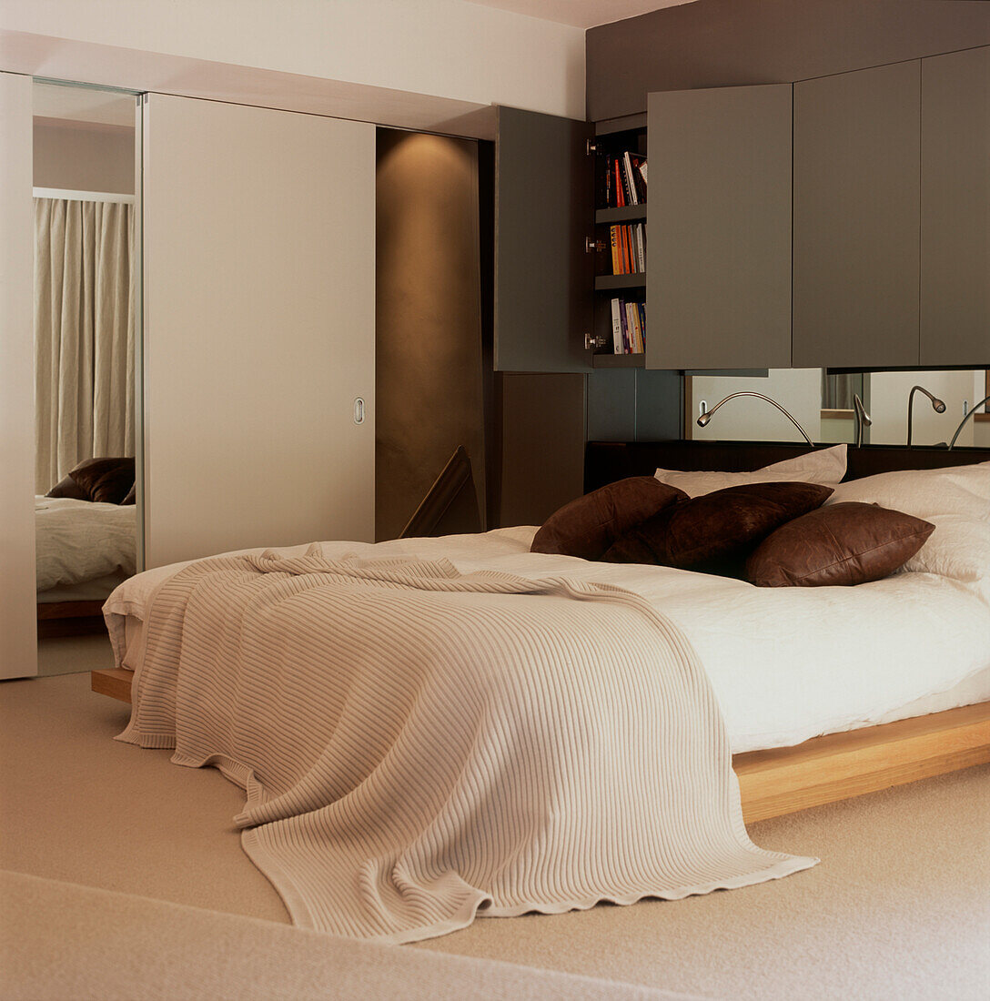 Doppelbett in einem maskulinen Schlafzimmer mit eingebautem Stauraum und Spiegelwand am Kopfende des Bettes