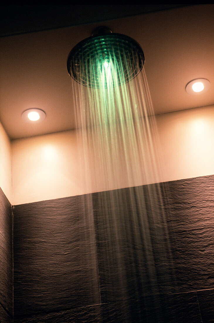 Shower head in slate tiled bathroom with green light reflected in the water