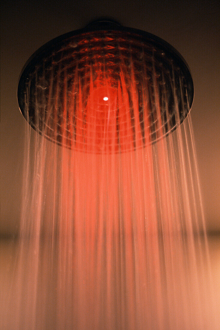Red light shining through water from shower head in bathroom