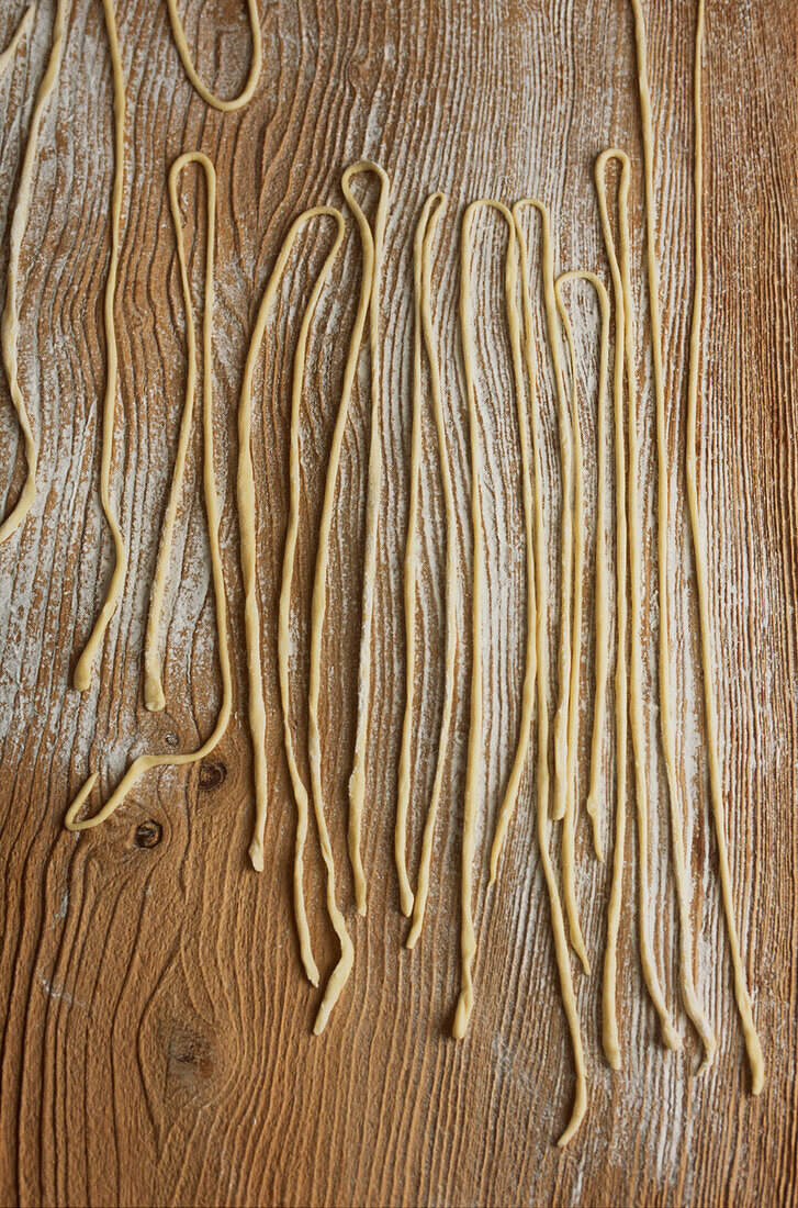 Freshly prepared noodles laid out on a floured wooden surface in a kitchen