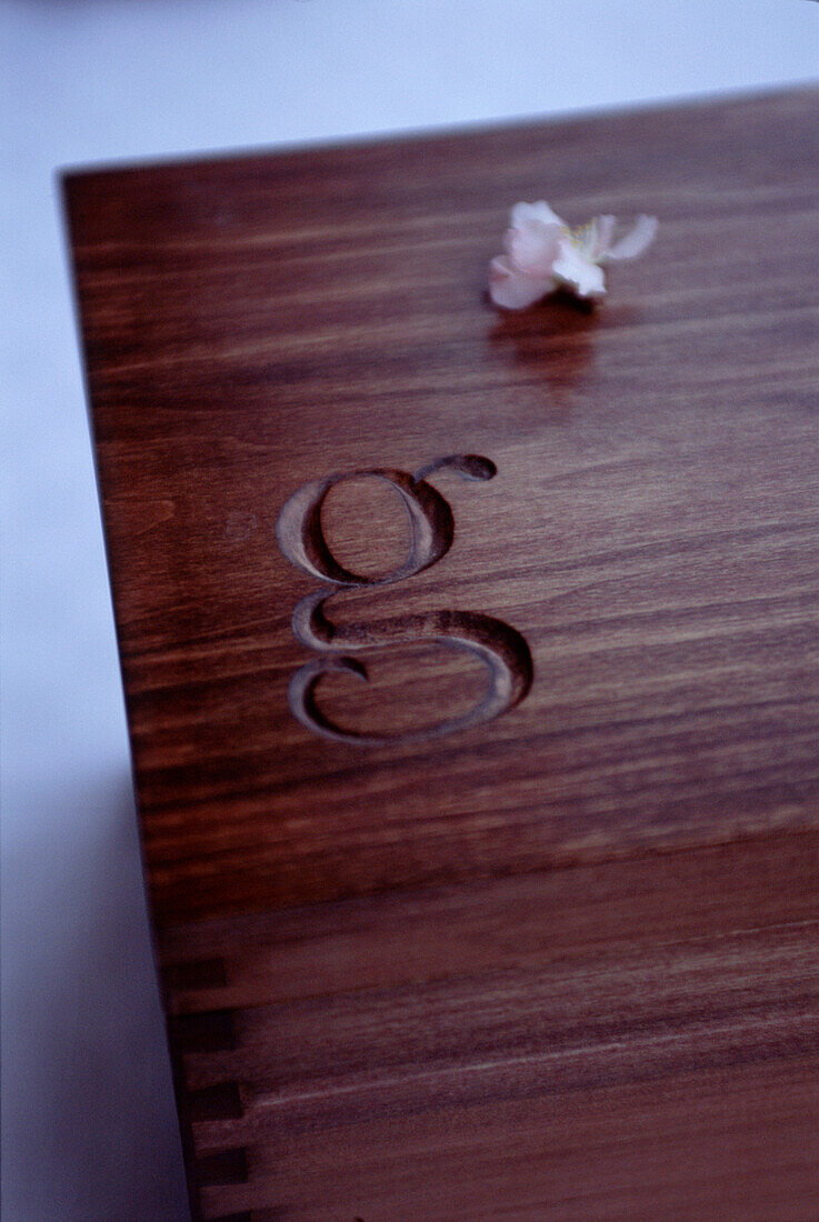 The letter 'g' carved into the top of a dark wooden box with a flower blossom alongside 