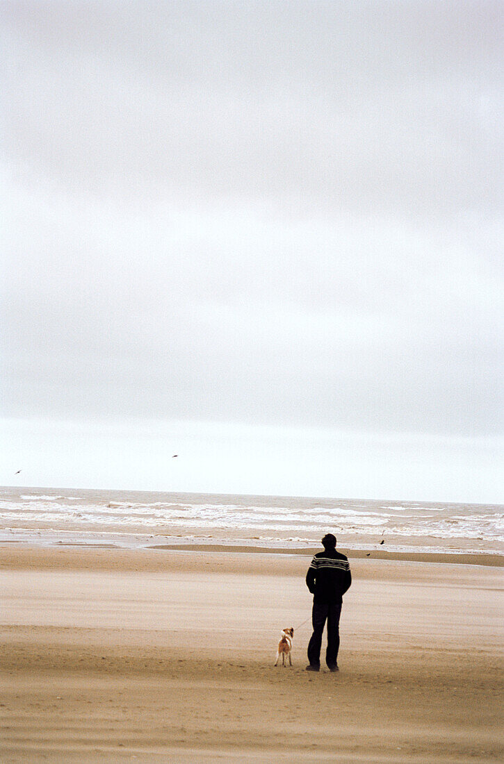 Man and dog looking out to sea on the beach 