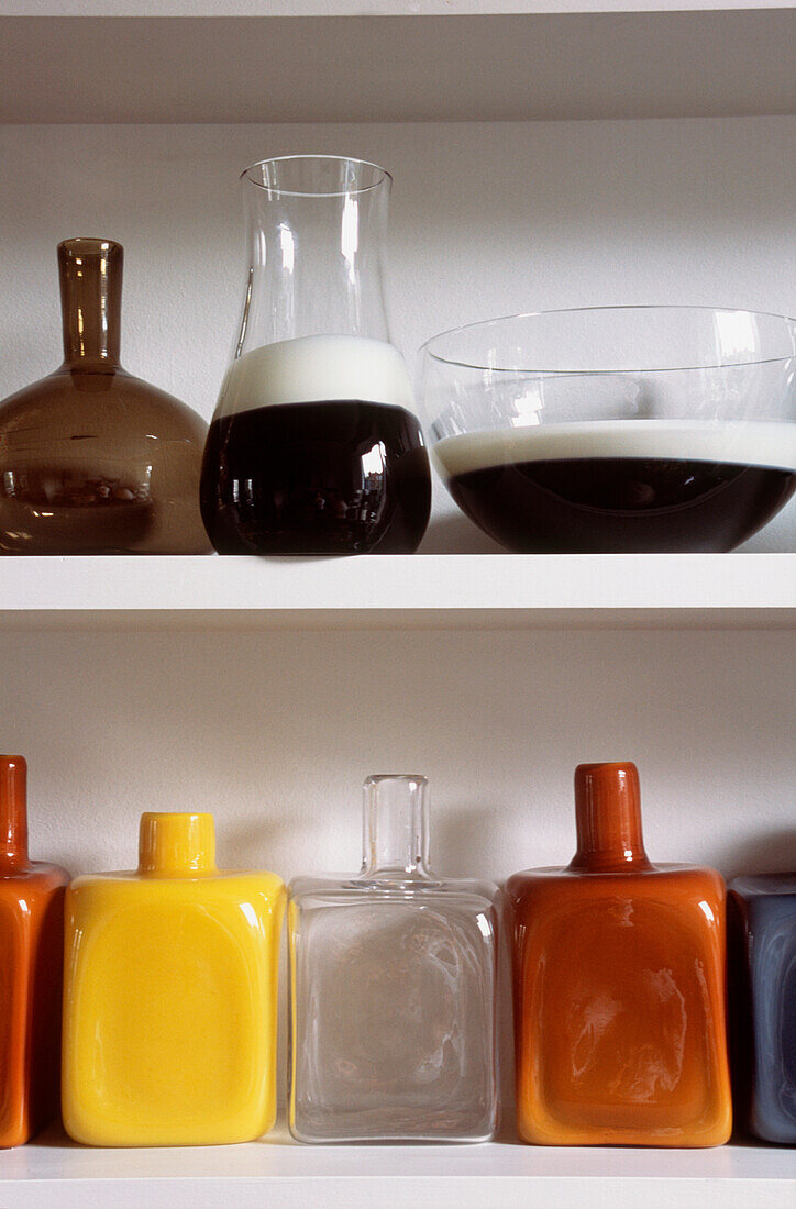 Detail von offenen Regalen mit einer Sammlung von bunten modernen Glaswaren, Vasen und Flaschen