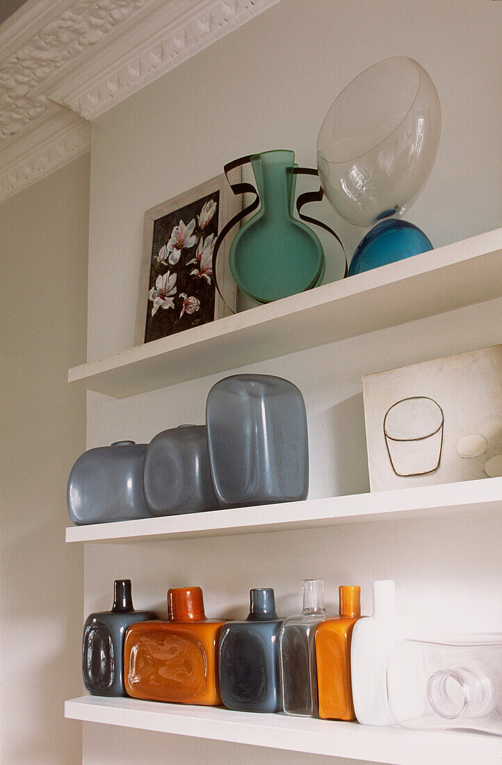Open shelves in living room with display of colourful glass bottles and vases