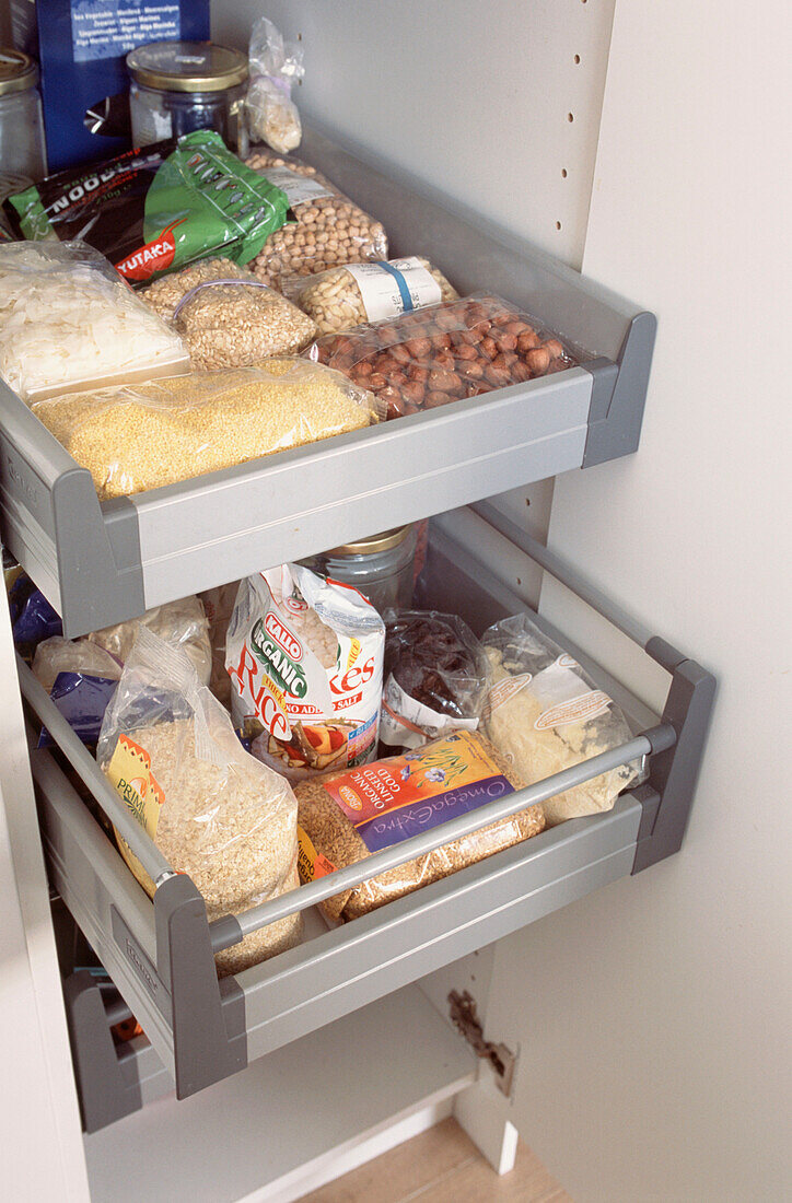 Offene Tür in einem Küchenschrank mit Schubladen, gefüllt mit Körnern, Hülsenfrüchten und Nüssen