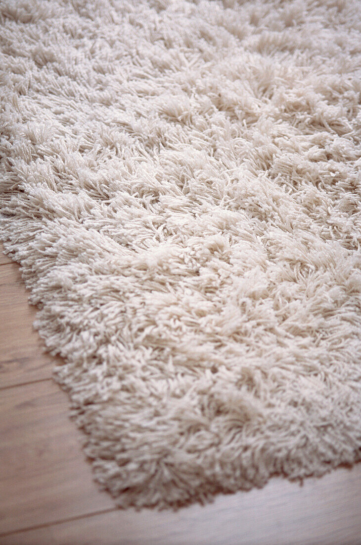 Detail eines weißen Zottelteppichs auf Holzboden
