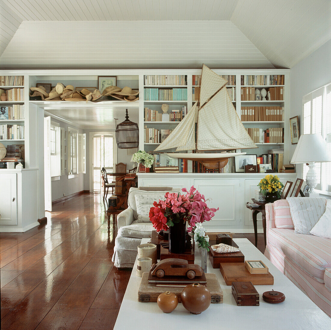 Offenes Wohn-Esszimmer mit eingebauten Bücherregalen und Schränken, in denen unter anderem Strohhüte und ein Modellsegelboot ausgestellt sind