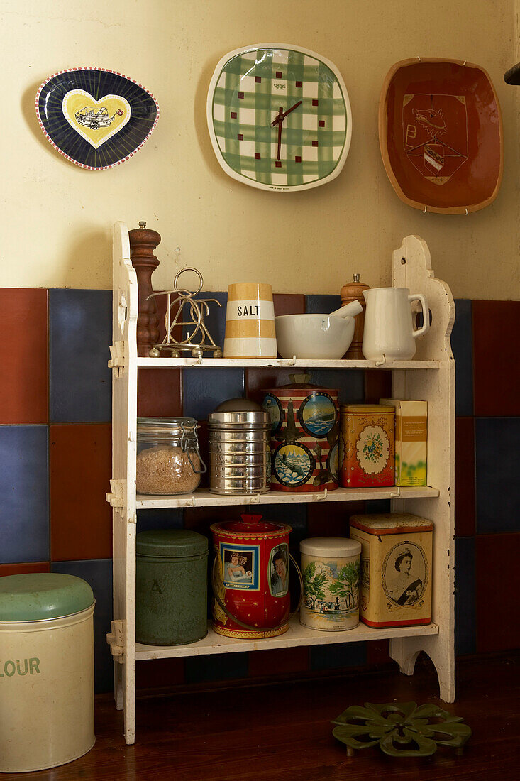 Detail von altem Küchengeschirr und Dosen auf offenen Regalen in der Küche mit an der Wand hängenden Tellern