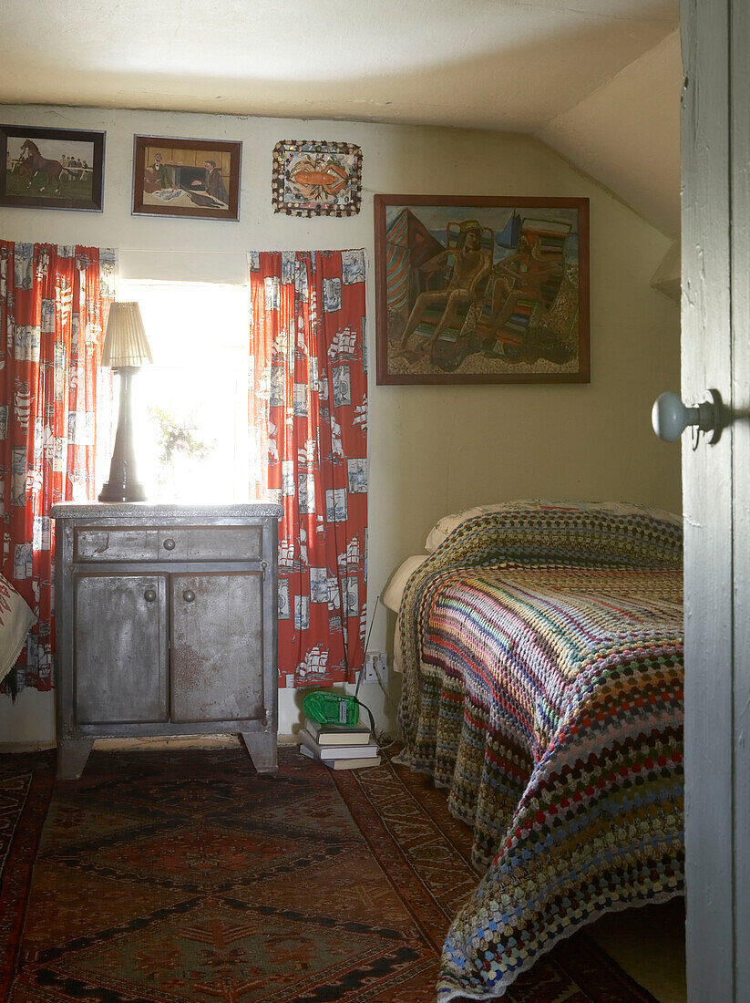 Gehäkelte Vintage-Decke auf einem Einzelbett mit Vintage-Stoffvorhängen und Kunstwerken