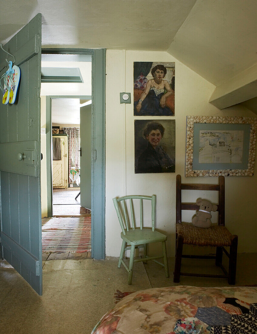 Two chairs by open door in bedroom with paintings and shell frame on wall 