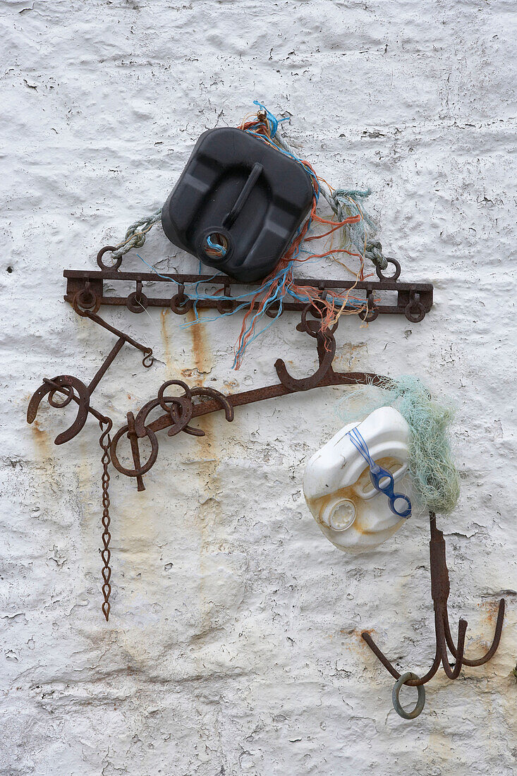White exterior wall with salvaged beach finds including plastic cans and metal items hanging
