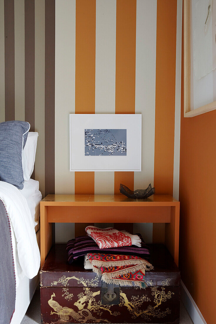 Gestreifte Wand im Schlafzimmer mit Druck über dem Nachttisch und orientalischer Truhe