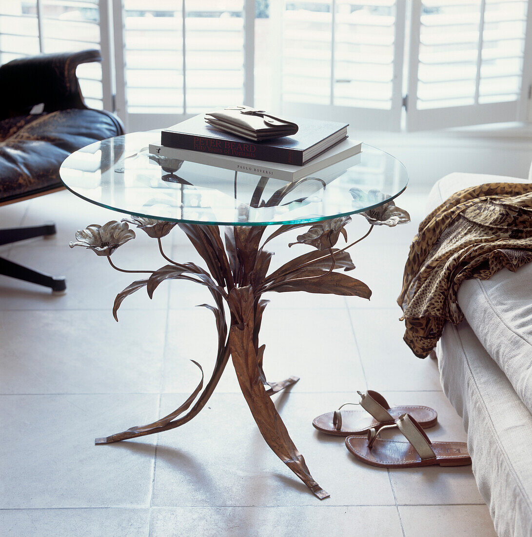Books and purse on circular glass topped coffee table with ornate decorative legs on floor tiles in living room