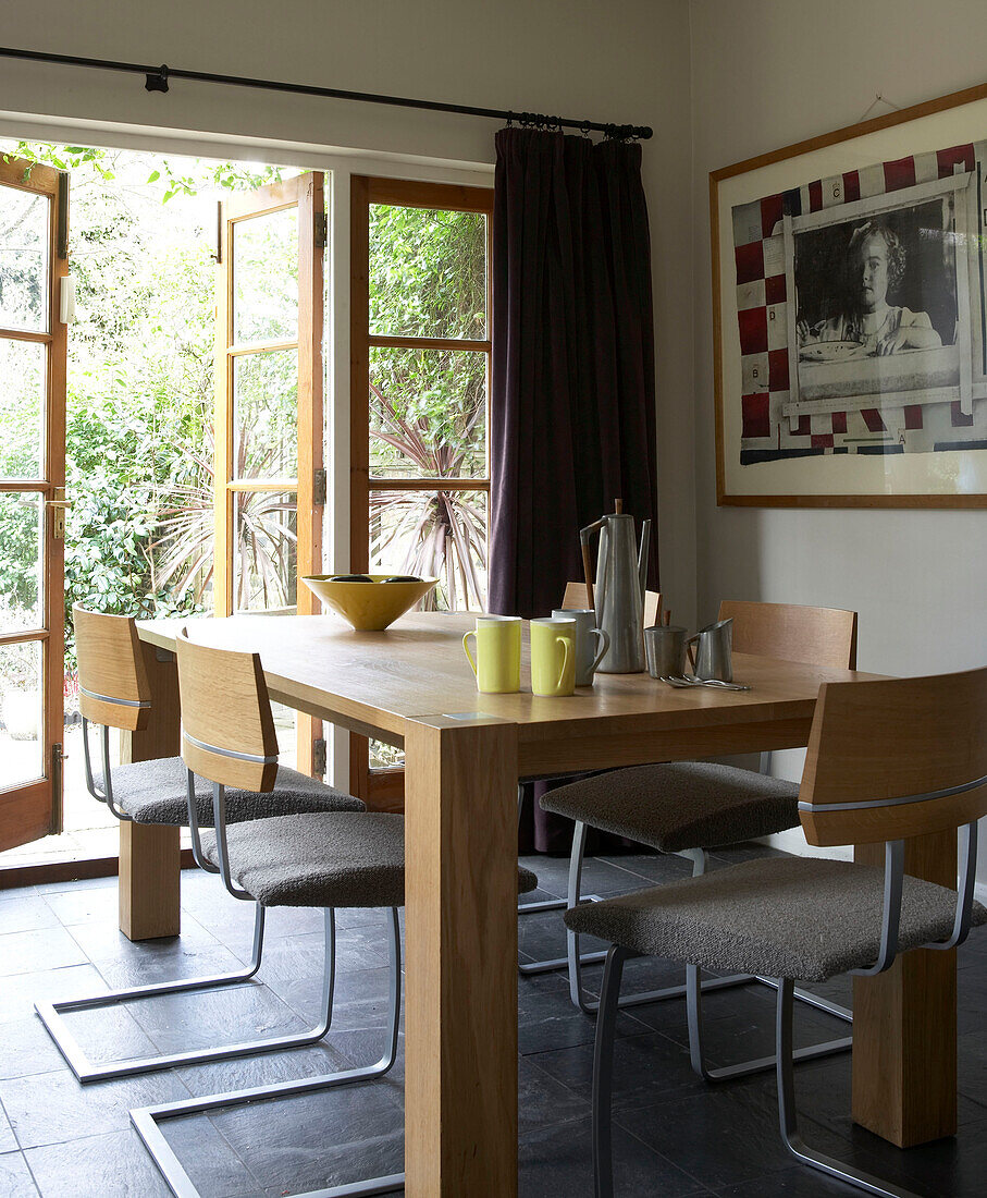 Pale wood dining table in grey tiled garden room of in London townhouse, UK