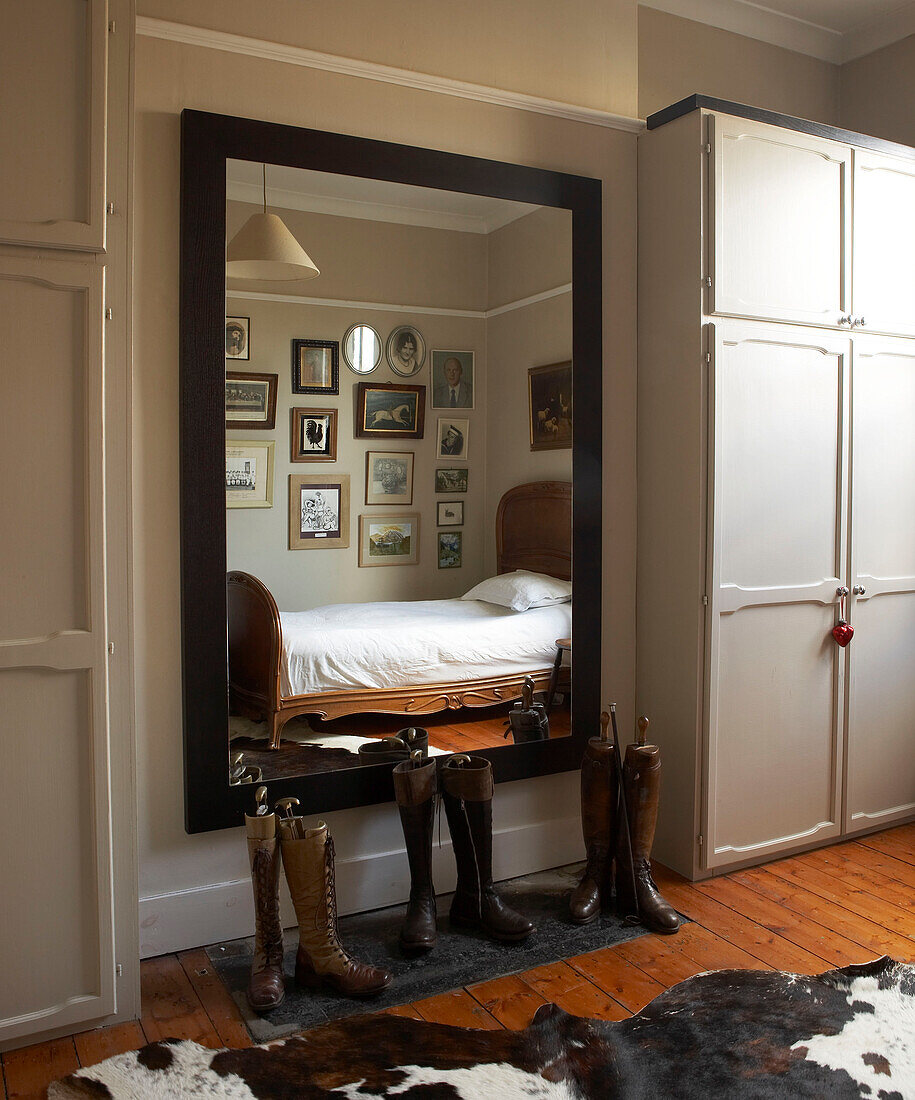 Reitstiefel und Einzelbett im Spiegel eines großen Schlafzimmerspiegels in einem Londoner Stadthaus, UK