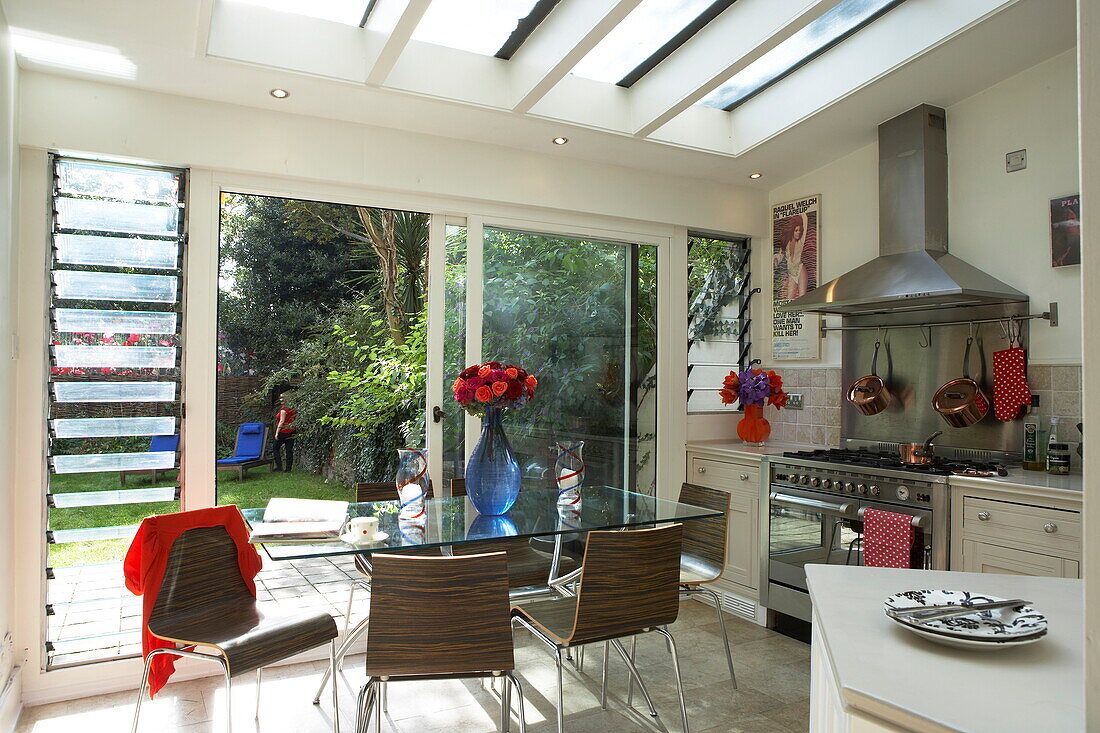 Glastisch in Londoner Küchenerweiterung mit Blick durch Schiebetüren in den Garten, England, UK