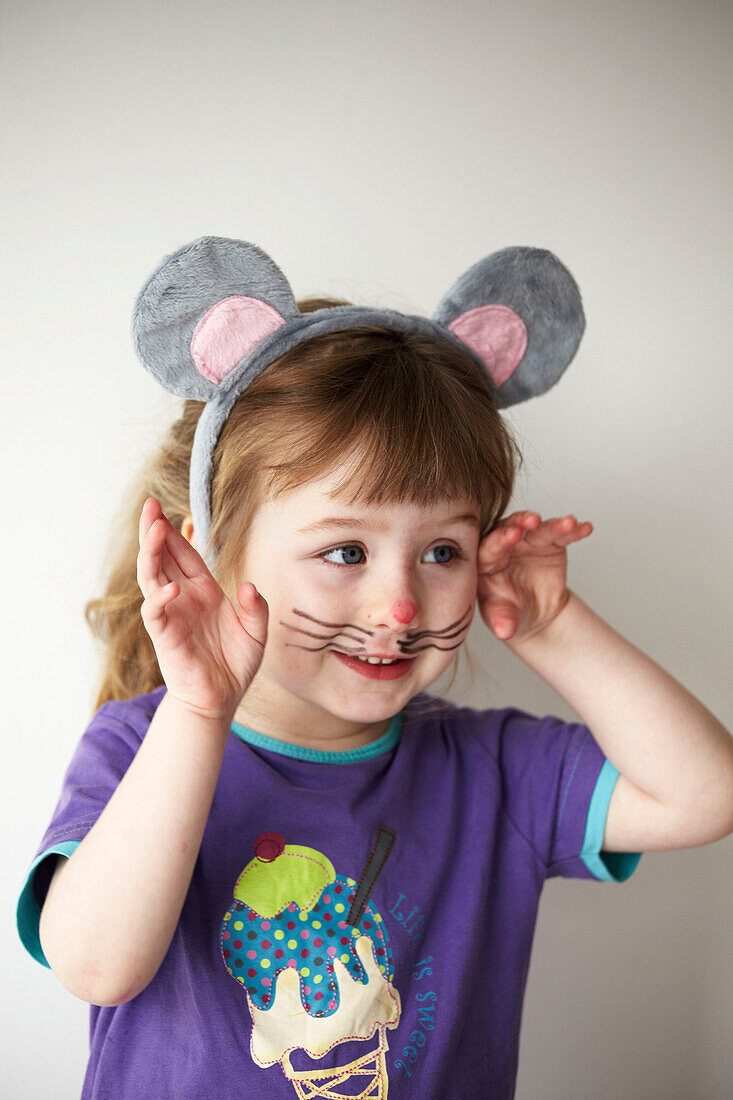 Kleines Mädchen mit lila T-Shirt, das sich eine Mäusemaske aufsetzt