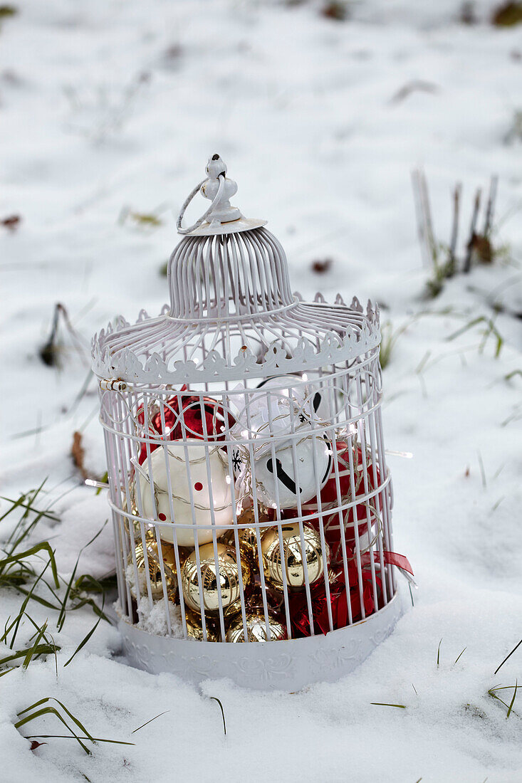 Weißer dekorativer Vogelkäfig mit Weihnachtsdekoration auf verschneitem Boden