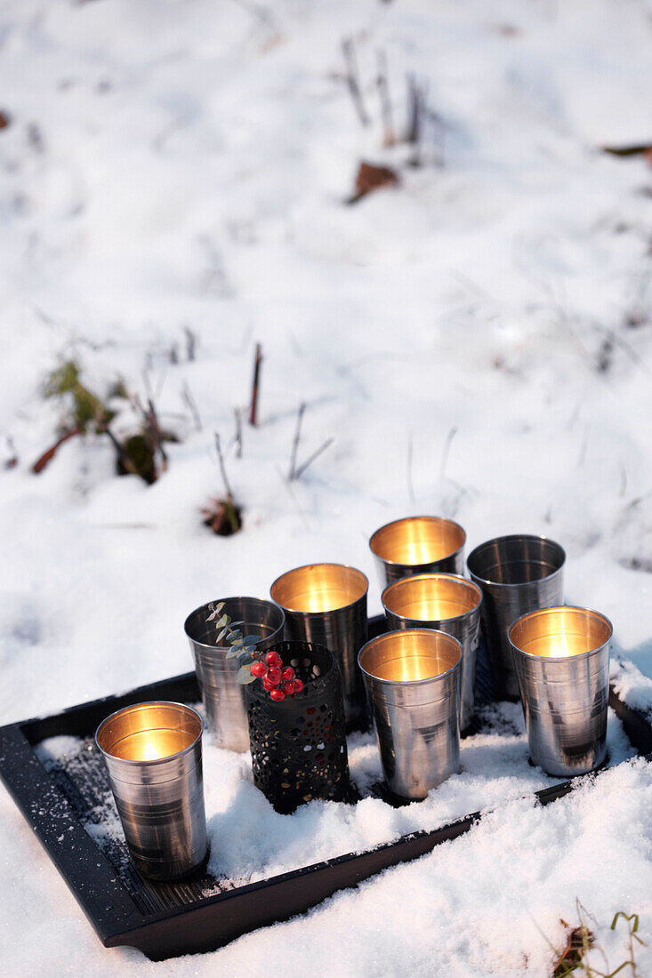 Metallische Teelichter auf einem Tablett im Schnee