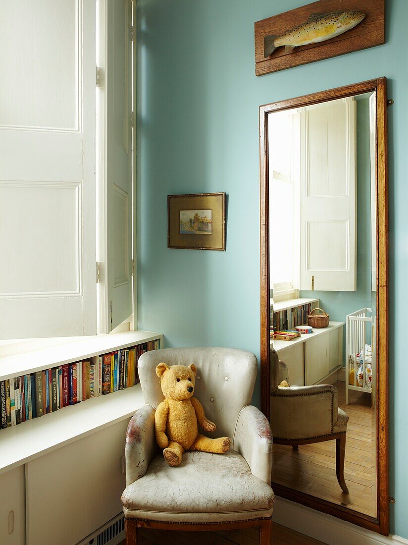 Teddybär auf einem Sessel in einer Zimmerecke mit Spiegel