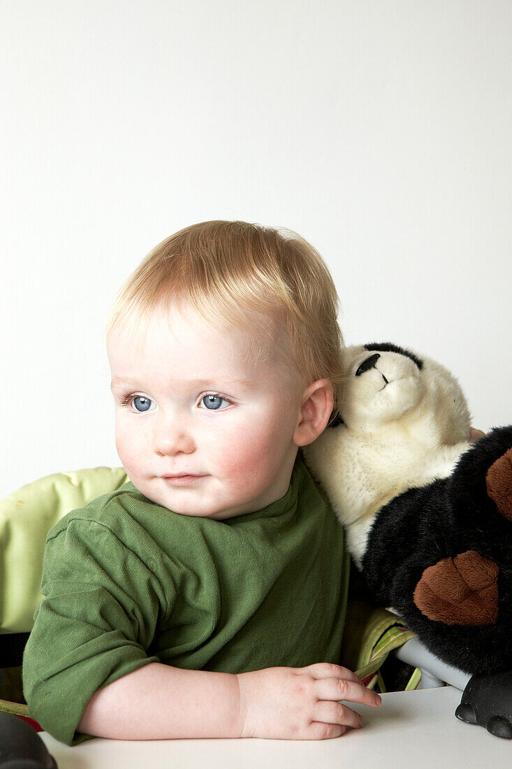 Two year old boy in green top sits with toy panda