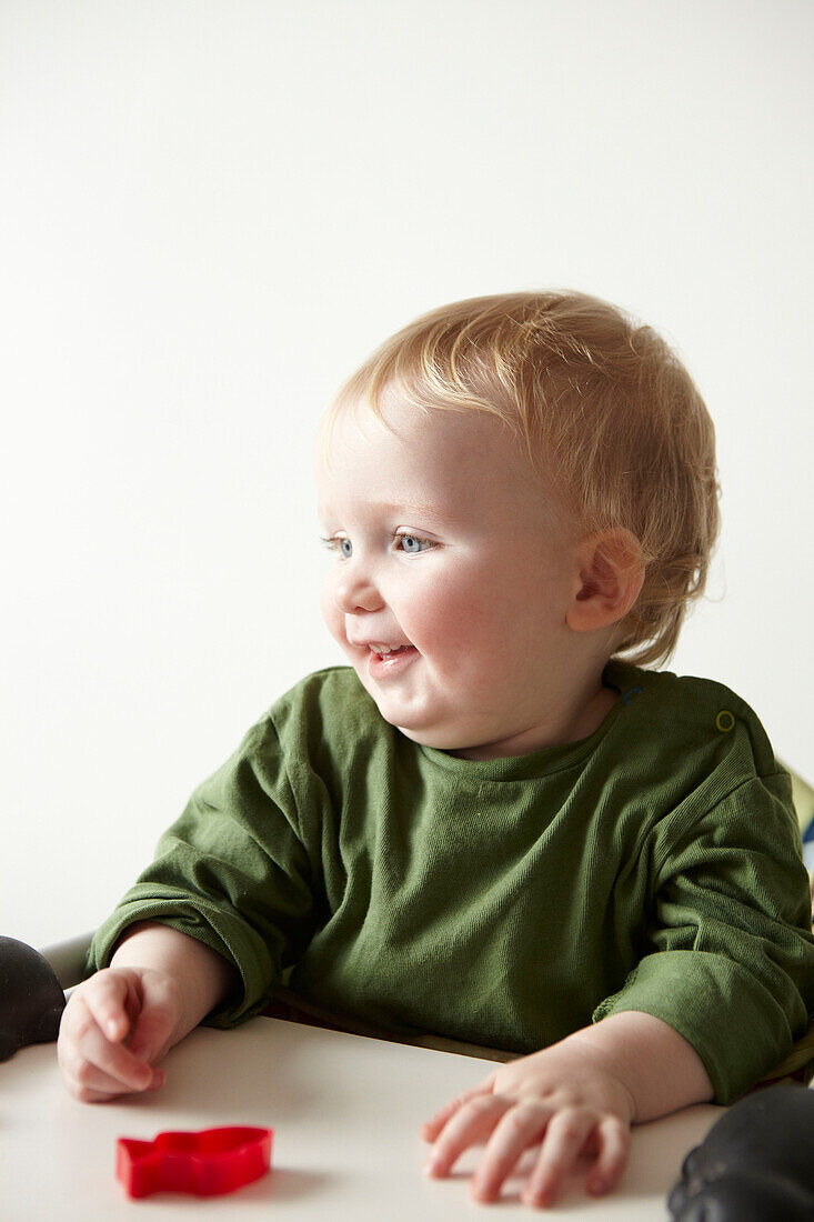 Zwei Jahre alter Junge in grünem Oberteil sitzt und spielt mit einem roten Spielzeug