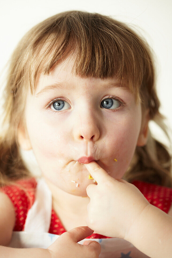 Drei Jahre altes Mädchen mit blauen Augen sitzt und lutscht an ihrem Finger
