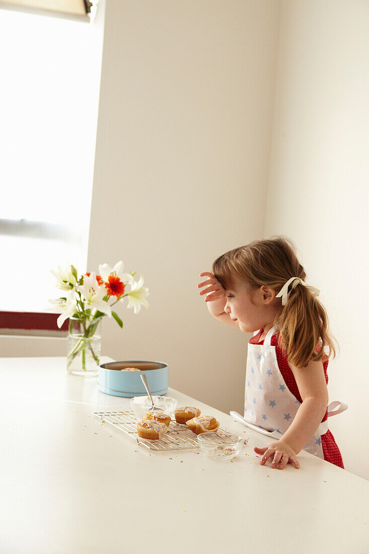 Three year old girl stands at cooling tray with her hand on her forehead