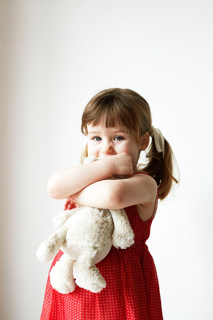 Junges Mädchen in rotem Kleid hält einen Teddybär